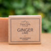 Image of a Three Hills Soap bar in Ginger Lime scent. The soap is labeled as a 'Recharging Scrubby' and features natural, eco-friendly packaging with a simple design. The background is blurred, highlighting the soap bar in the foreground.