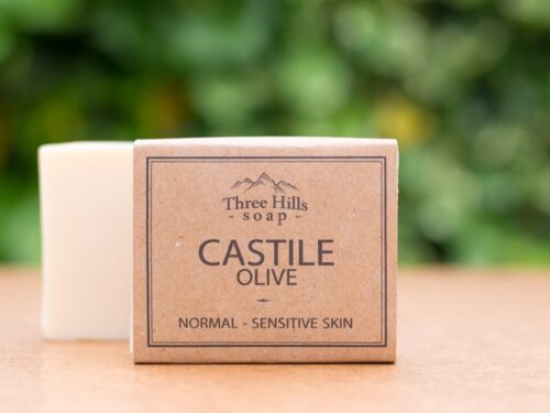Castile Olive soap bar with rustic label on light surface and green outdoor background