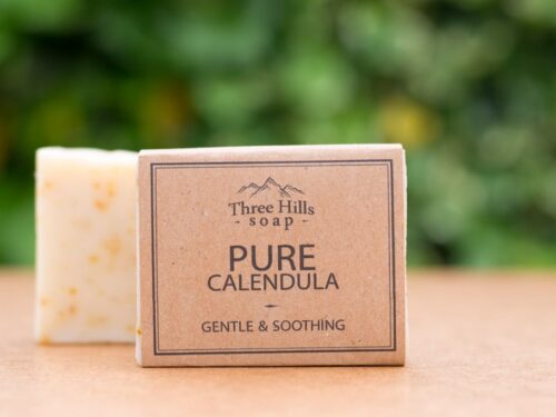 Pure Calendula soap bar with rustic label on light surface and green outdoor background