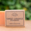 Image of a Three Hills Soap bar in Sweet Orange Spearmint scent. The soap is labeled 'Sweet & Balancing' and features natural, eco-friendly packaging with a simple design. The light orange soap bar is positioned in the foreground with a blurred, green background.