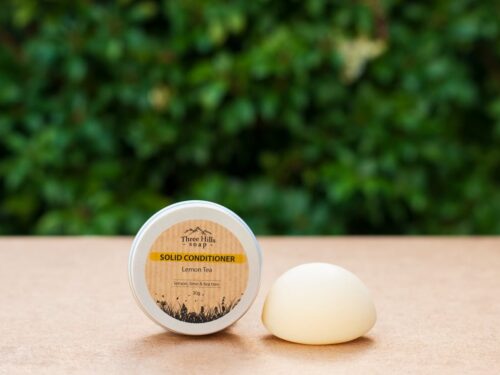 Solid conditioner bar and tin on wooden table with green blurred background