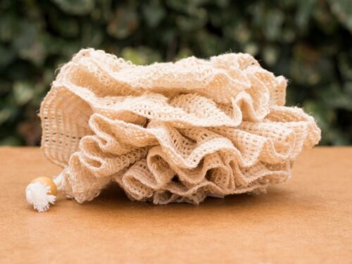 Natural shower puff with cotton loop on wooden surface and green background