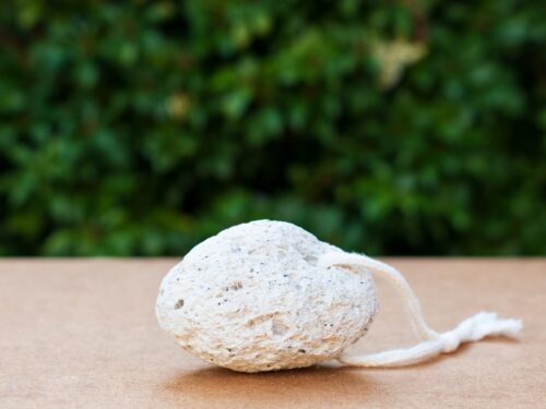 Natural pumice stone with cotton loop on flat surface and green blurred background