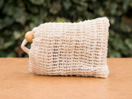 Natural sisal soap bag with a wooden bead placed on wooden surface and green background