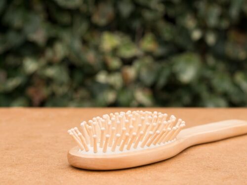Wooden hairbrush with rounded bristles on natural surface and green leafy background