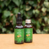 Two bottles of Three Hills Soap Nourishing Beard Oil, one with a dropper and one with a screw cap, placed on a wooden surface with a green leafy background.