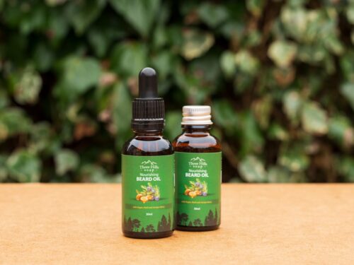 Two bottles of Nourishing Beard Oil on wooden surface with green leafy background