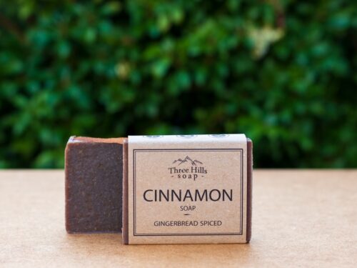 Cinnamon soap bar with rustic label on light surface and green outdoor background