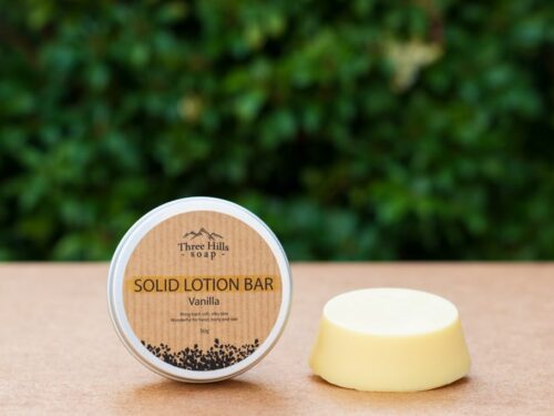 Vanilla solid lotion bar and labeled tin on flat surface with green blurred background