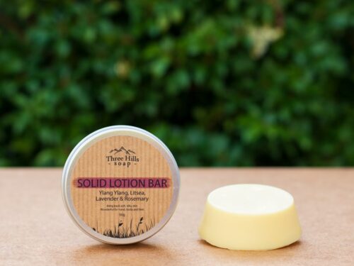 Ylang Ylang solid lotion bar and labeled tin on flat surface with green blurred background