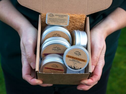 Person holding open box of Three Hills Soap tins outdoors with natural fiber packaging