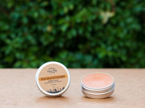 Open tin of Sea Buckthorn herbal balm with lid beside it on flat surface