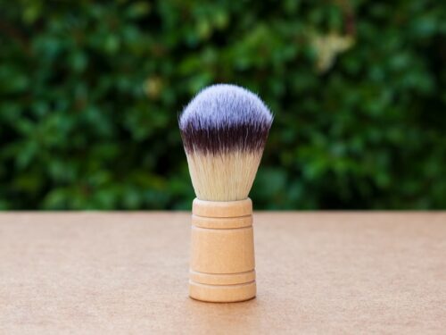 Shaving brush with wooden handle and dense bristles on surface with green background
