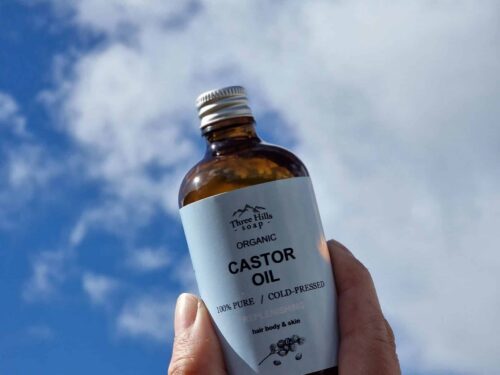 Hand holding a bottle of Organic Castor Oil by Three Hills Soap against a blue sky