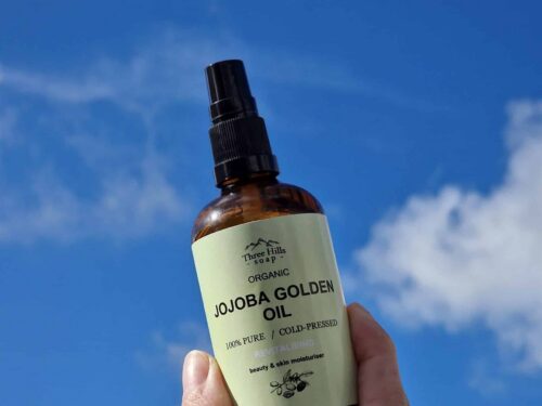 Bottle of Three Hills Soap Organic Jojoba Golden Oil with clear sky background