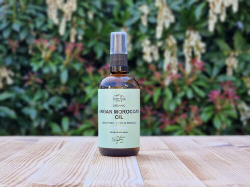 Three Hills Soap Organic Argan Moroccan Oil in 100ml amber glass bottle with pump, displayed on wooden table outdoors