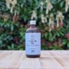 Three Hills Soap Organic Castor Oil in 100ml amber glass bottle with silver cap, displayed on outdoor wooden surface with green foliage background