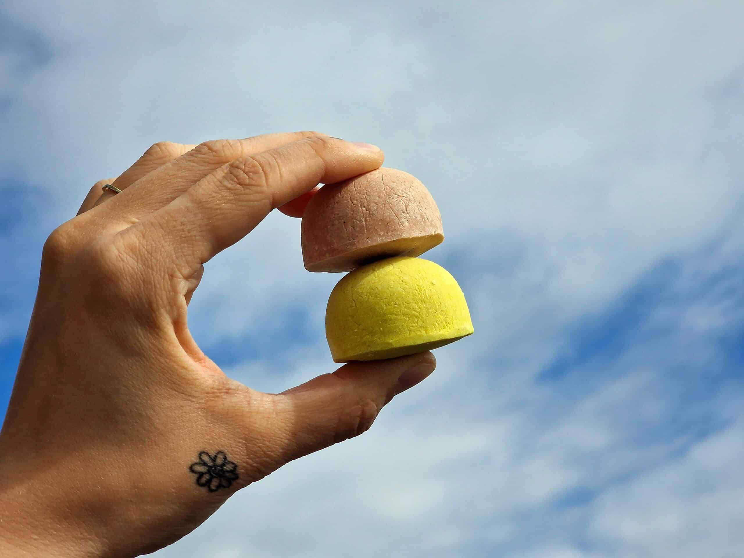 Hand holding two three hills shampoo bars against sky